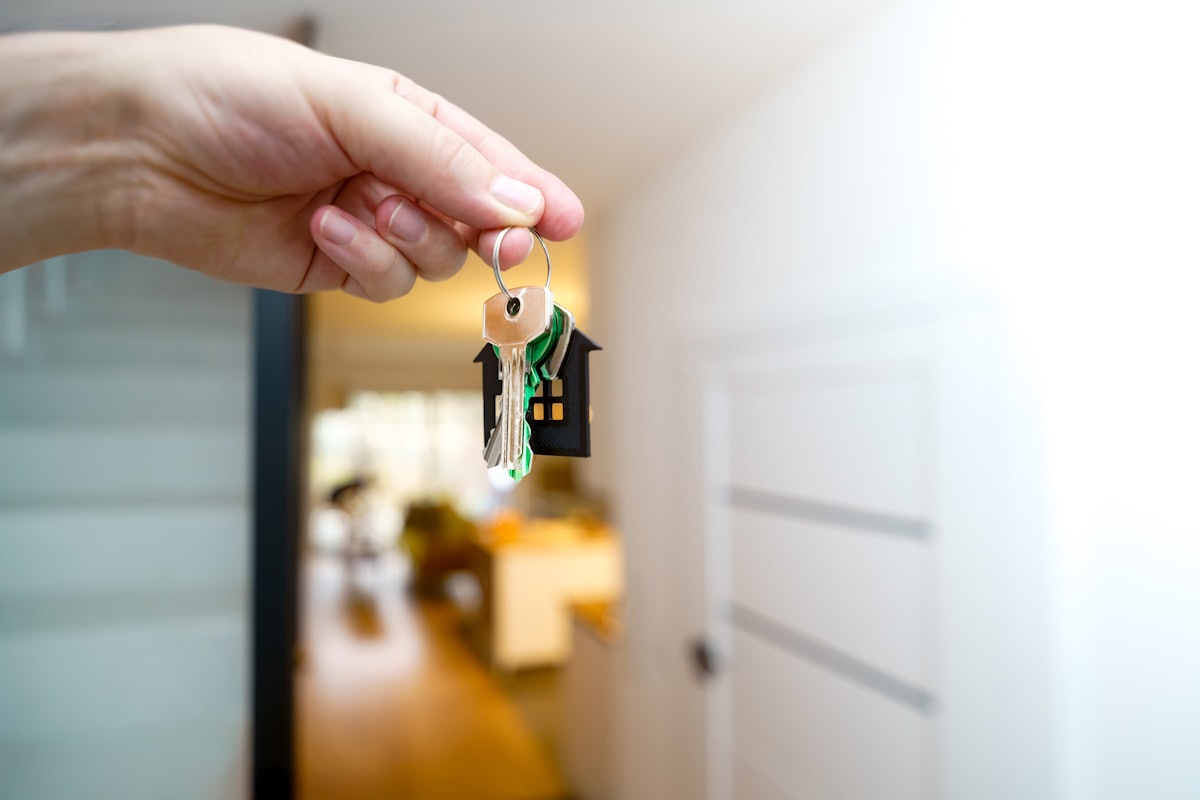 Hand übergibt einen Wohnungsschlüssel mit Haus-Anhänger